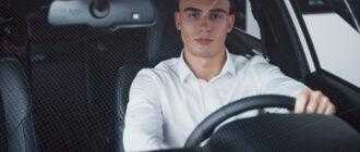 young man sits newly bought car holding his hands rudder